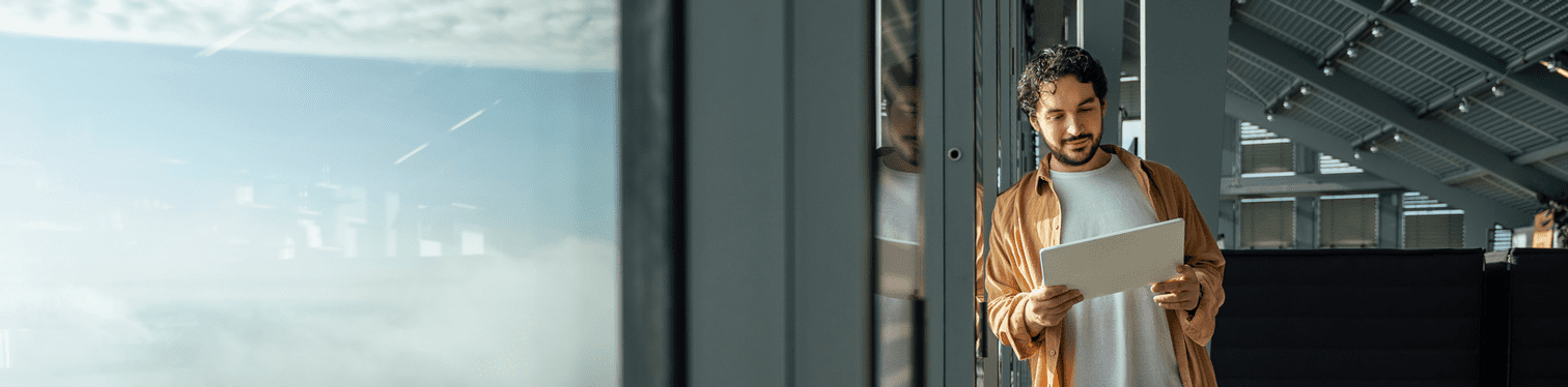 Individual reading data on a tablet inside a glass-walled office space.