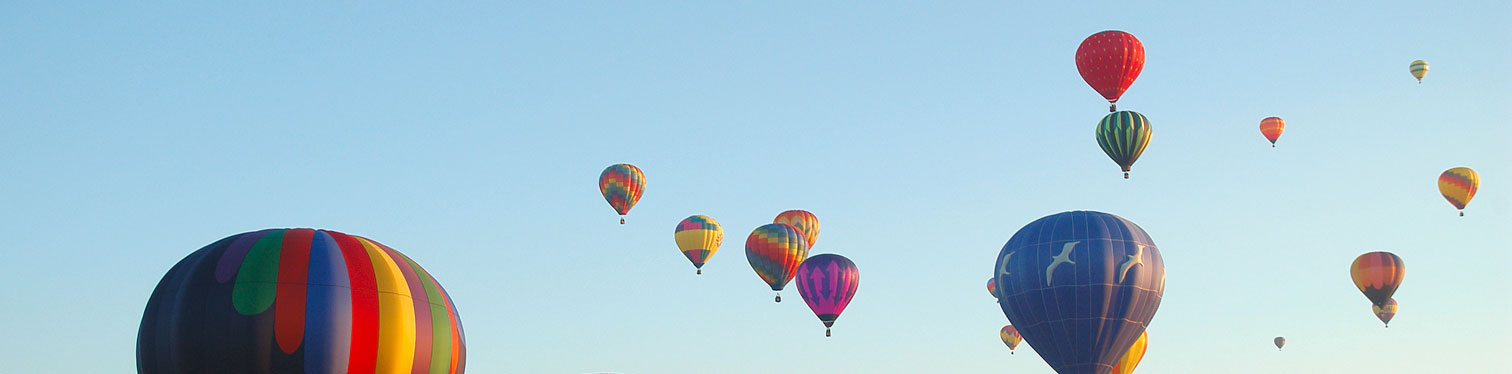 Colorful hot air balloons of different sizes floating against a clear blue sky, with one large striped balloon in the foreground.