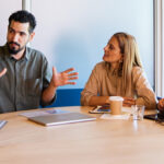 A diverse team of six professionals seated around a conference table, engaged in discussion during a collaborative meeting in a modern office.