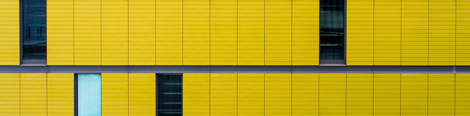 Modern building façade with bright yellow paneling and narrow vertical windows in a geometric pattern.