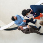 Aerial view of five business professionals collaborating on a walkway, discussing strategy on a tablet, representing cross-functional evaluation of agentic AI tools.