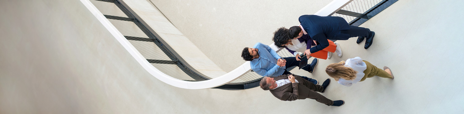 Aerial view of five business professionals collaborating on a walkway, discussing strategy on a tablet, representing cross-functional evaluation of agentic AI tools.